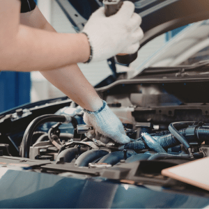 technician holding flashlight and working under the hood of a car