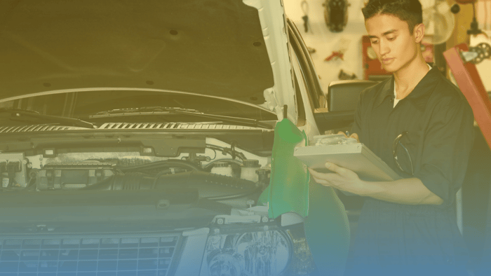 young technician writing on clipboard next to car with open hood