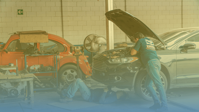two technicians working on a car with one under the car and the other standing beside the car
