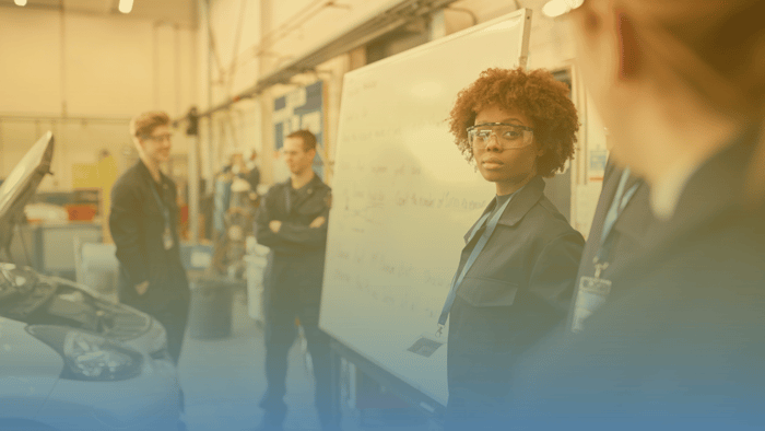 group of technicians standing around a white board and a car with an open hood