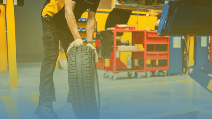 technician rolling tire in shop next to car on a lift 