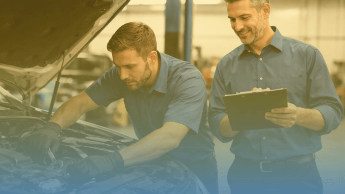 manager with clipboard overlooking technician working on car